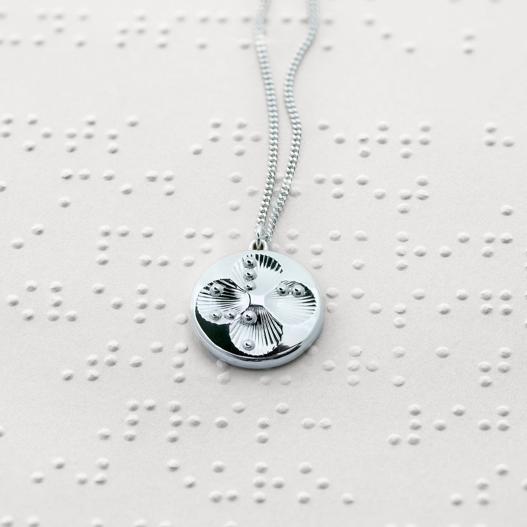 Lucky Dots lucky charm resting on a Braille text paper, its 50 cm silver curb chain elegantly curving across the page.
