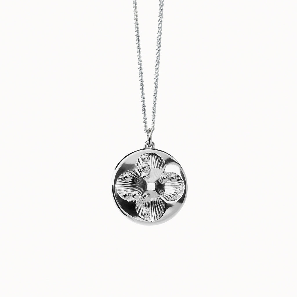 Close-up of the Lucky Dots silver pendant hanging from its silver curb chain against a white background. The four shallow circular dips form a subtle four-leaf clover, and the chain is broad, flat, and interlinked, characteristic of a classic curb style.